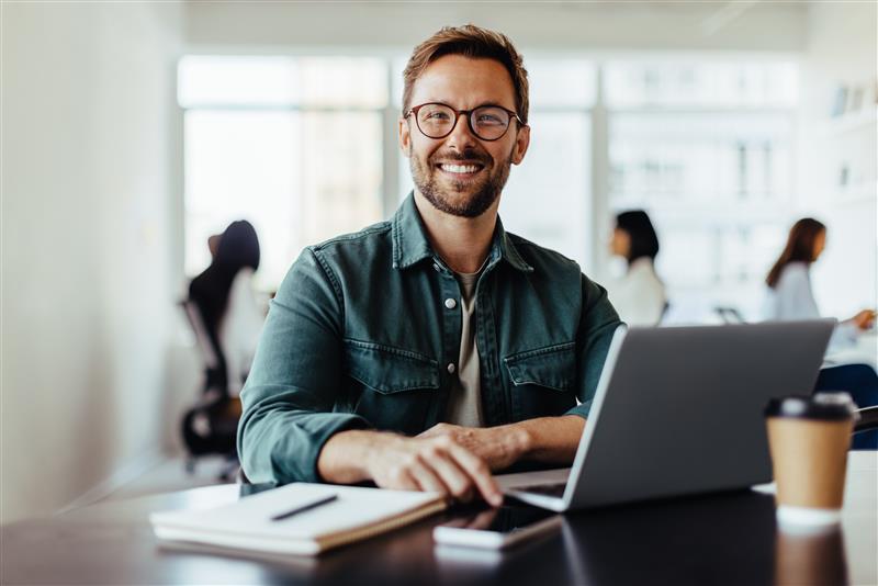 smiling-man-with-glasses-working-on-laptop-in-office.jpeg