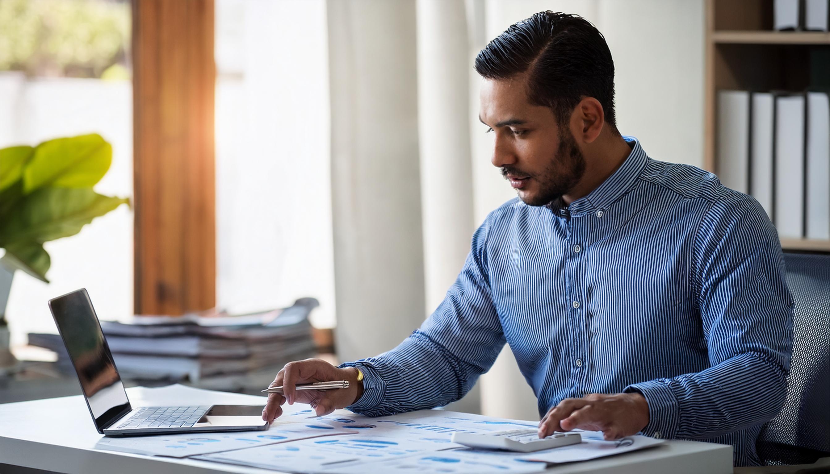 man-in-blue-shirt-reviewing-charts-at-desk-with-laptop.jpeg