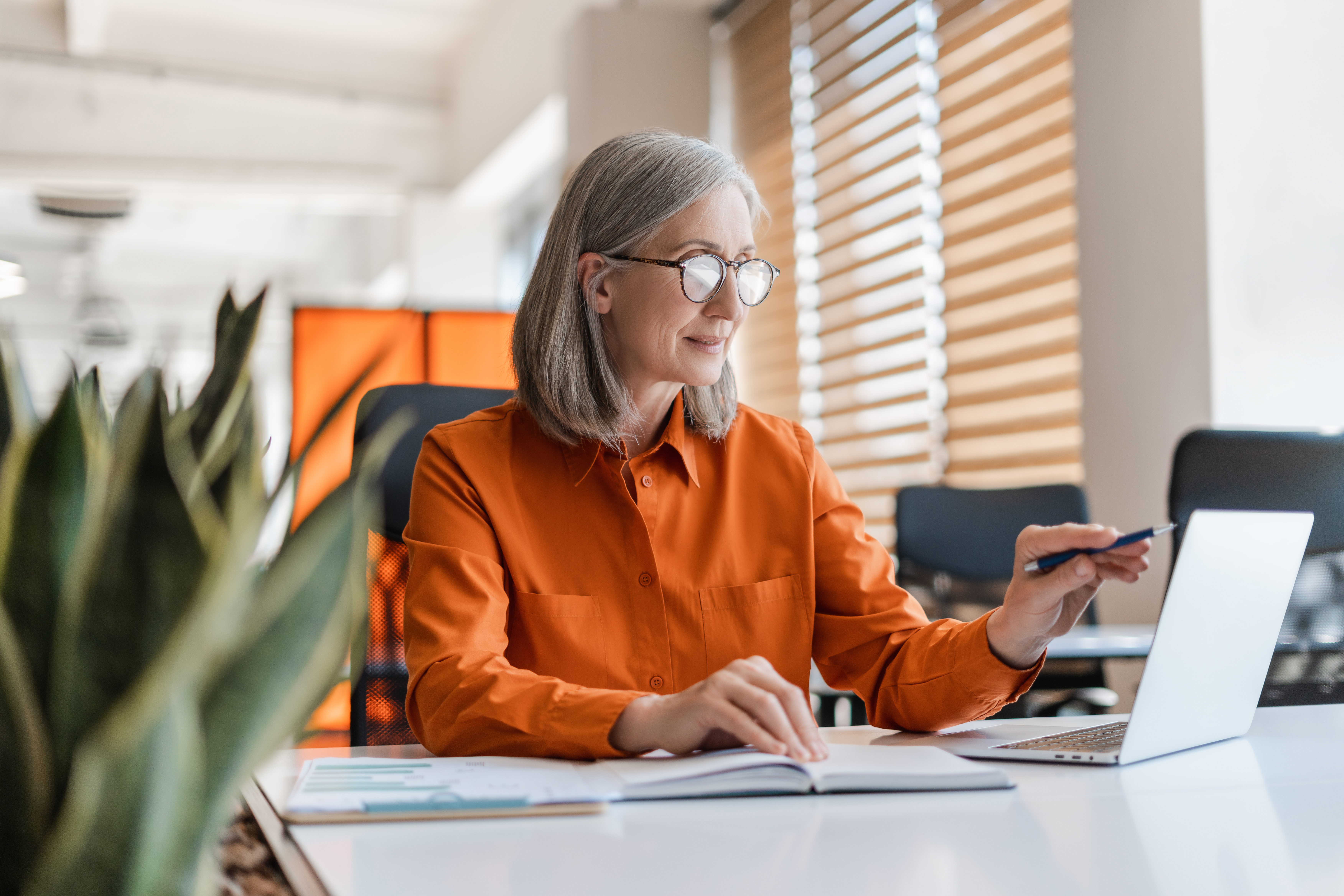 senior-woman-with-glasses-working-on-laptop-in-orange-shirt.jpeg