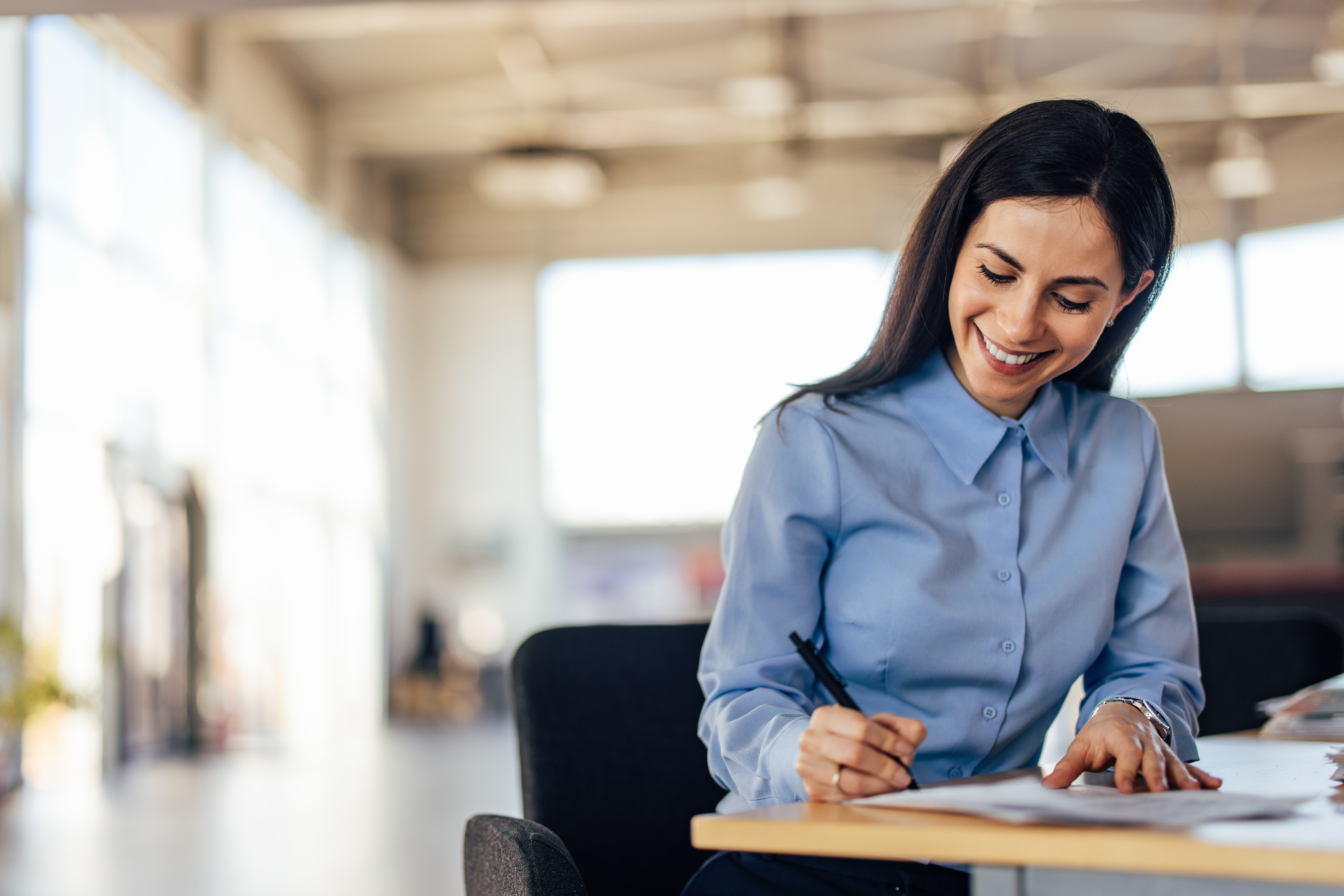 smiling-businesswoman-writing-notes-at-office-desk.jpeg