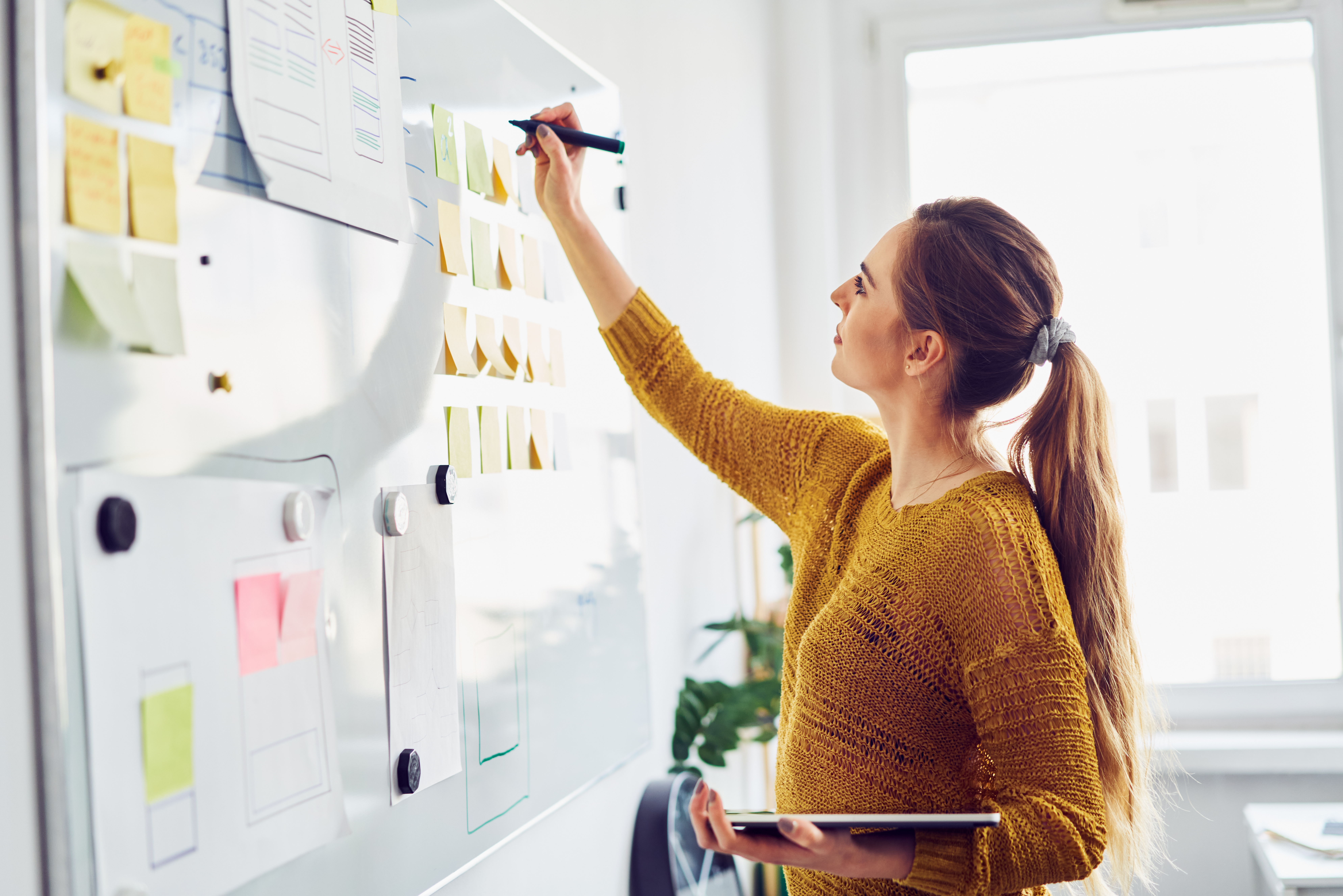 woman-writing-on-whiteboard-with-sticky-notes-and-tablet.jpeg